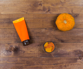 Cosmetic fall flatlay with beauty products, coffee scrub and orange pumpkin on a brown wooden background.