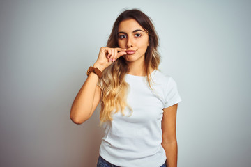 Fototapeta premium Young beautiful woman wearing casual white t-shirt over isolated background mouth and lips shut as zip with fingers. Secret and silent, taboo talking
