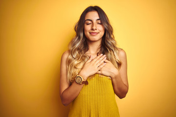 Young beautiful woman wearing t-shirt over yellow isolated background smiling with hands on chest with closed eyes and grateful gesture on face. Health concept.