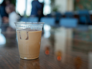 Iced coffee inside clear plastic cup sitting on counter of busy coffee shop