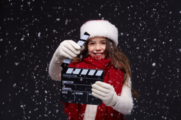Young beautiful smiling girl in knitting pullover holding director's clapper board for making Christmas video in studio.Movie production clapper board.Lights, camera, action. Start of winter holidays.