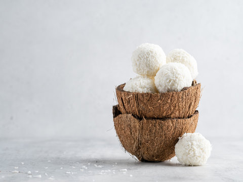 Coconut bliss balls in coconut shells on white gray background closeup view
