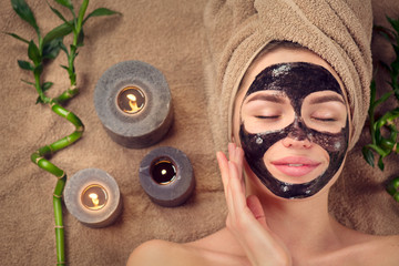Beautiful woman with black purifying black charcoal mask on her face. Beauty model girl with black...
