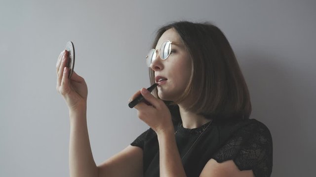 Beautiful confident woman doing makeup before fashing show holding lipstick and eyelash with hand mirror. Fashion and style concept