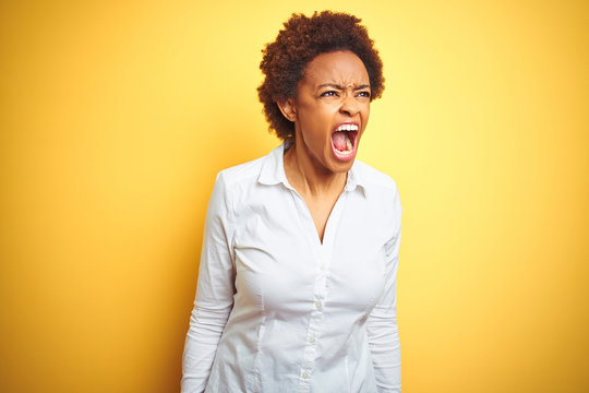 African american business woman over isolated yellow background angry and mad screaming frustrated and furious, shouting with anger. Rage and aggressive concept.