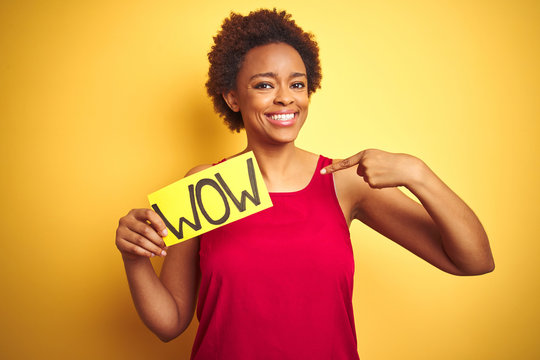 Young african american woman showing wow banner board over yellow isolated background with surprise face pointing finger to himself