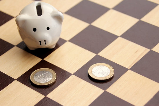 piggy piggy bank and euro coins in the form of figures on a chessboard, business concept, games, close-up, copy space