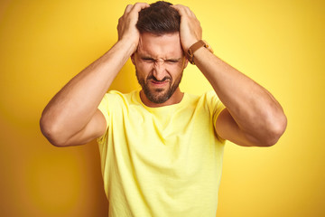 Fototapeta na wymiar Young handsome man wearing casual yellow t-shirt over yellow isolated background suffering from headache desperate and stressed because pain and migraine. Hands on head.