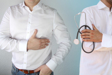 man in a white shirt holds on to his chest in the heart area, next is a doctor in a white coat with...
