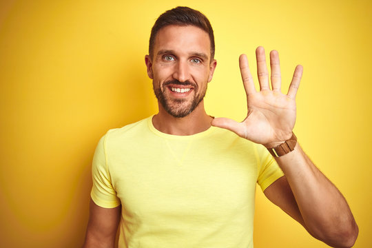 Young handsome man wearing casual yellow t-shirt over yellow isolated background showing and pointing up with fingers number five while smiling confident and happy.