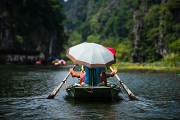 Obraz premium A vietnamese local rows a rowing boat with his feet for tourists as they travel on a boat tour through the limestone caves of Ninh Binh