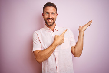 Young handsome man wearing elegant summer shirt over pink isolated background amazed and smiling to the camera while presenting with hand and pointing with finger.