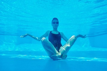 Young athletic woman sitting in lotus pose underwater in swimming pool