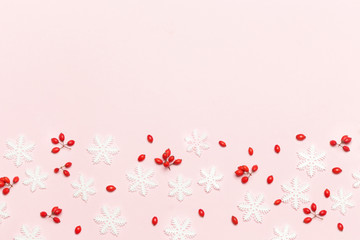 Elegant winter background with copy space. Red berries and snow flakes on pale pink background. 
