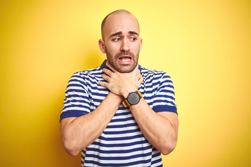 Young bald man with beard wearing casual striped blue t-shirt over yellow isolated background shouting and suffocate because painful strangle. Health problem. Asphyxiate and suicide concept.