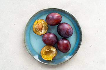 Ripe plums lie on a blue plate. Pieces of purple plum.