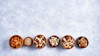 pecans, hazelnuts, almonds, pine nuts, Brazil nut, cashews in wooden bowls on blue background, top...