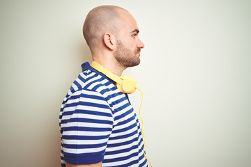 Young man listening to music wearing yellow headphones over isolated background looking to side, relax profile pose with natural face with confident smile.