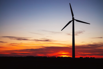 Windmills for electric power production at sunset in a field