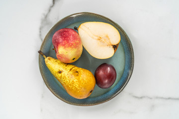Ripe autumn fruits lie on a blue plate. Apple, pear and plum on a marble background.