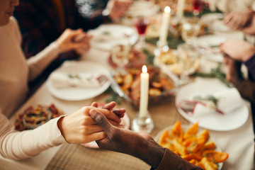 Closeup of people sitting at dining table on Christmas and joining hands in prayer, copy space