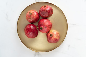 Red pomegranate lies on a golden tray in the background a marble slab. Exotic ingredient of tropical juice.