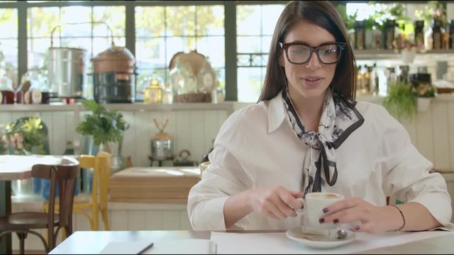 Beautiful caucasian businesswoman with eyeglasses sitting in cafe, drinking coffee and usig laptop.