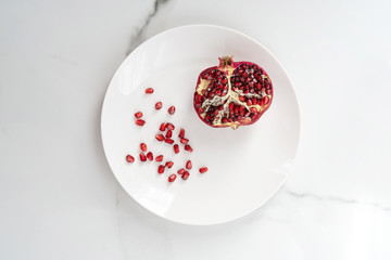 The cut pomegranate lies on a white background. Close-up of the center of a pomegranate. An ingredient of exotic juice. Pomegranate particles on a marble background.