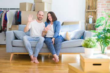 Fototapeta na wymiar Young couple sitting on the sofa arround cardboard boxes moving to a new house showing and pointing up with fingers number ten while smiling confident and happy.