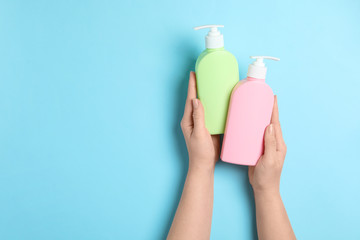 Woman holding blank bottles of cosmetic products on blue background, top view. Space for design