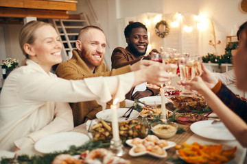 Multi-ethnic group of people raising glasses while celebrating Christmas with friends and family...