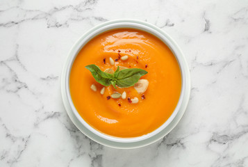 Delicious pumpkin soup in bowl on marble table, top view