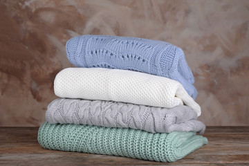 Stack of folded knitted sweaters on wooden table against brown background