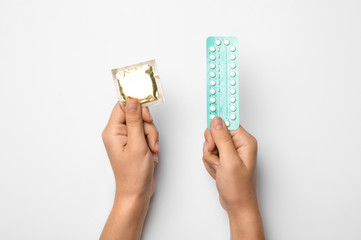 Woman holding condom and birth control pills on white background, top view. Safe sex
