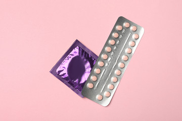 Condom and birth control pills on pink background, top view. Safe sex