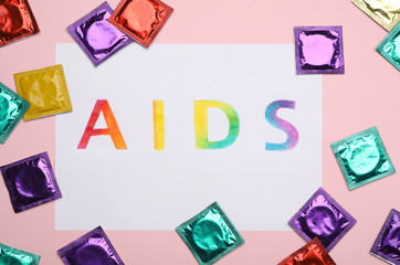 Colorful condoms and paper sheet with word AIDS on pink background, flat lay. Safe sex