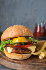 Fresh juicy bacon burger on wooden board against grey background