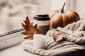 Cup of coffee, pumpkin, dried autumn leaves on window. Autumn composition.