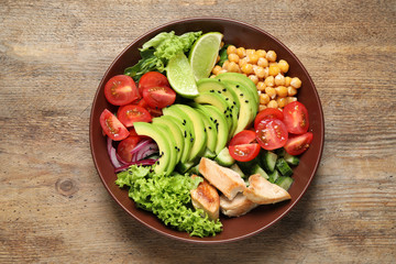 Delicious avocado salad with fried chicken on wooden table, top view