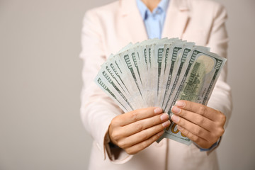 Young woman holding dollar bills on light grey background, closeup