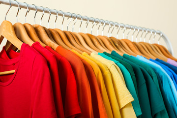 Rack with bright clothes on light background. Rainbow colors