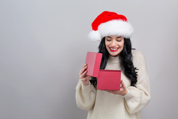 Fototapeta na wymiar Young woman with santa hat opening a Christmas gift box on a gray background