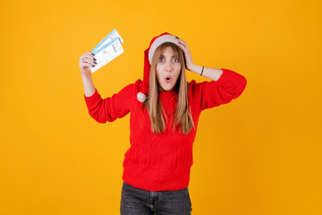 happy woman holding airplane tickets wearing santa hat isolated over yellow