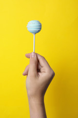 Woman holding sweet cake pop on yellow background, closeup