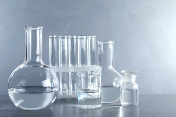Laboratory glassware with liquid samples for analysis on table against grey background