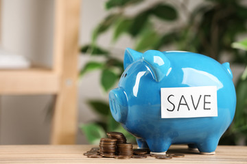 Piggy bank with word SAVE and coins on wooden table against blurred background
