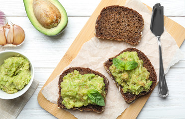 Flat lay composition with tasty avocado sandwiches on white wooden table