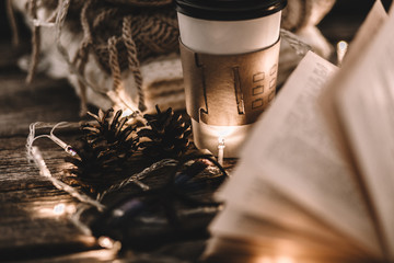 Winter composition. Cup with coffee, garland, book, cones on a wooden background.