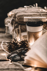 Winter composition. Cup with coffee, garland, book, cones on a wooden background.