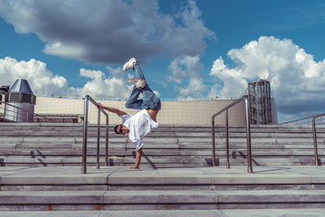 strong male dancer, standing on one arm in jump, dancing breakdance, summer city, background cloud stairs, hip-hop break dancer. Youth lifestyle, , trendy, modern, fitness sport, positive motivation.